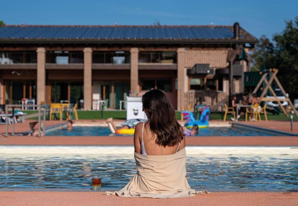 a woman sitting on the beach near a swimming pool at Incanto Glamping village in Savio di Ravenna