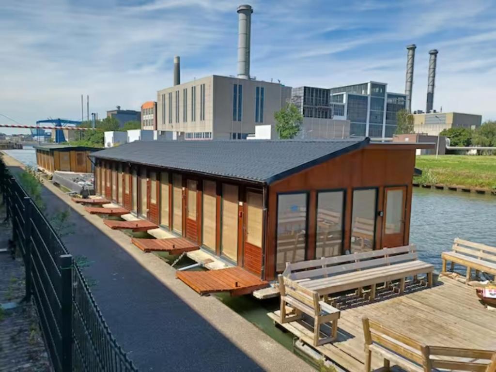 a building on the side of a river with benches at Off-Grid Boat Experience - Stay Zero Footprint in Utrecht