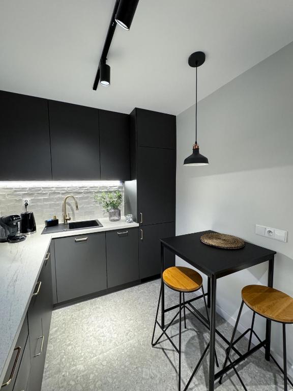 a kitchen with black cabinets and a table and two stools at Apartament Cieszynka in Ciechanów