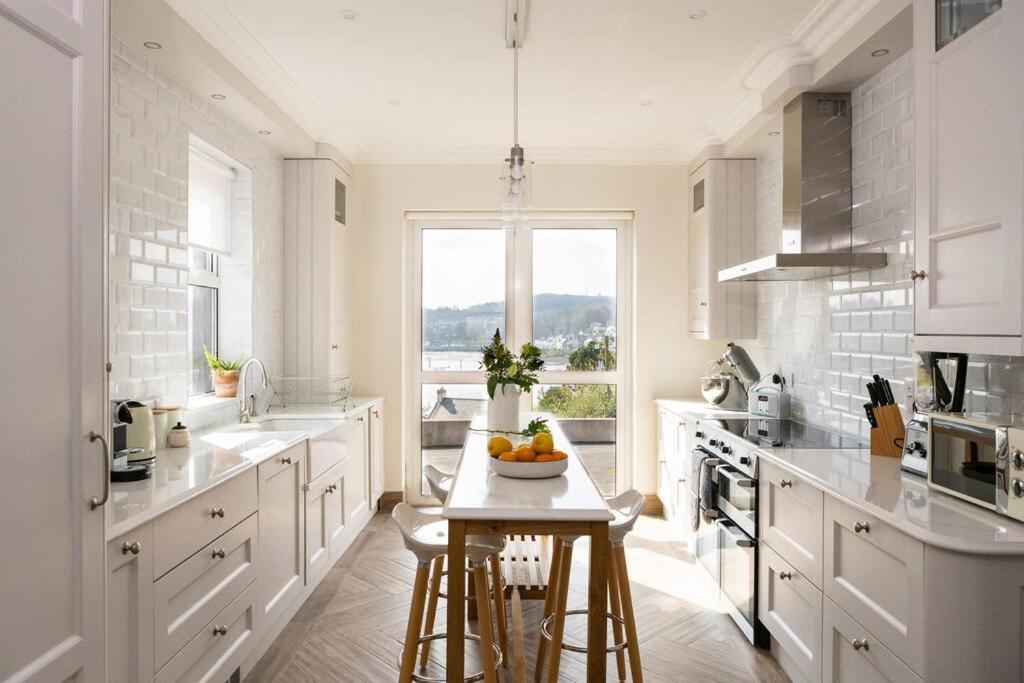 a white kitchen with a table with a bowl of fruit on it at Luxury Waterfront House in Cobh