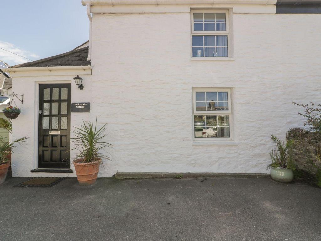a white house with a door and two windows at Blacksmiths Cottage in Newquay