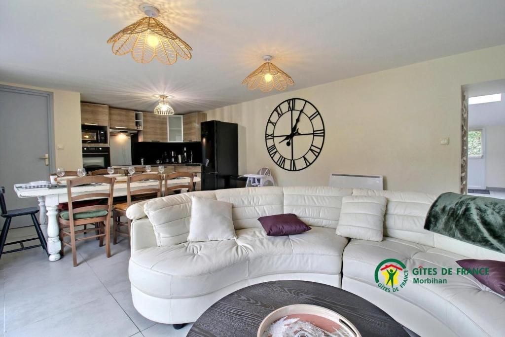 a living room with a white couch and a clock on the wall at Au charme des bois in Plouhinec