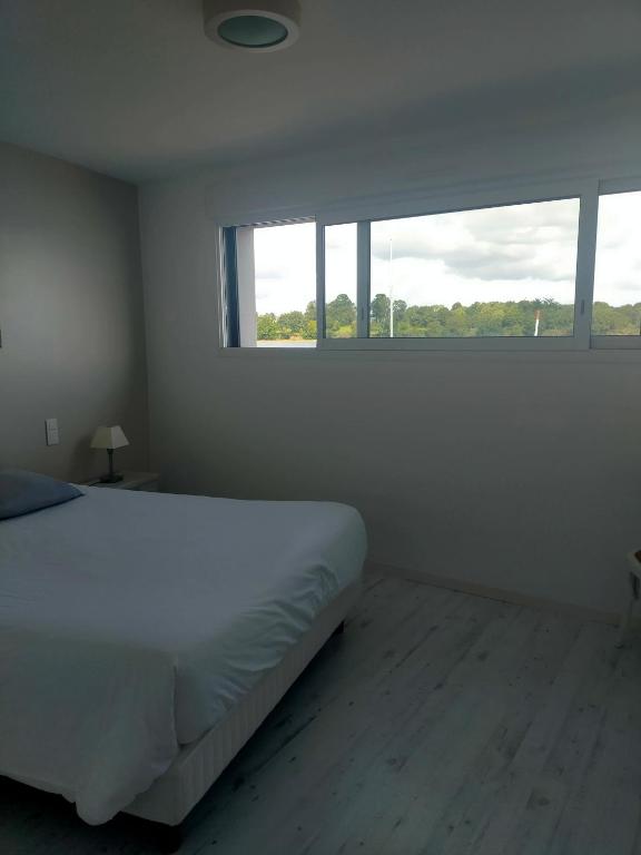 a white bedroom with a bed and two windows at Location les pieds dans l'eau in Vannes