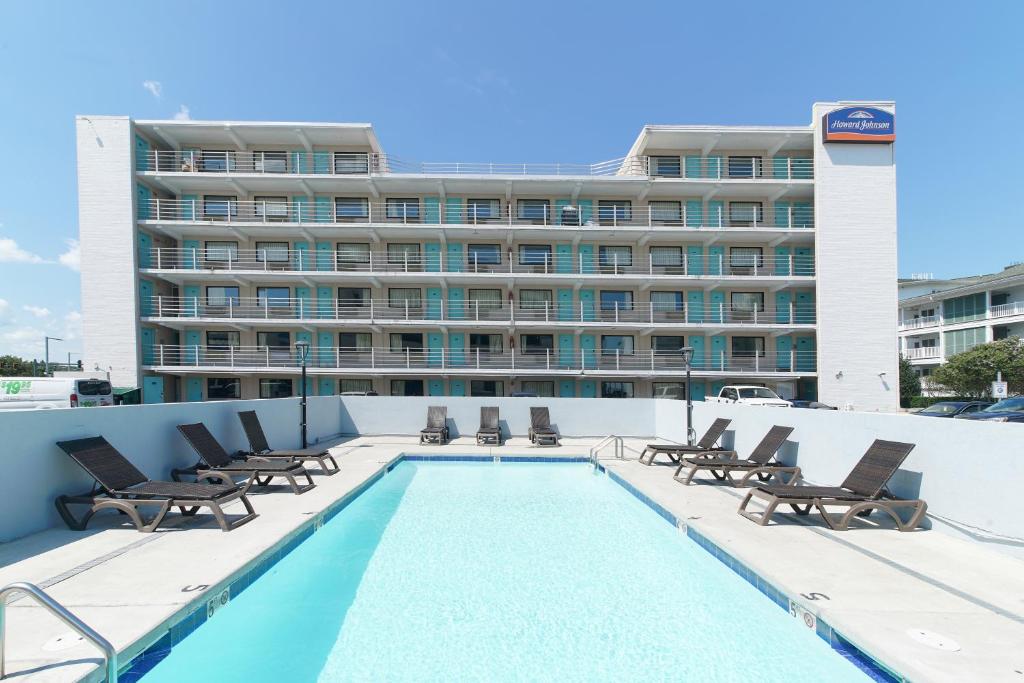 a hotel with a swimming pool and chairs and a building at Howard Johnson by Wyndham Virginia Beach At The Beach in Virginia Beach