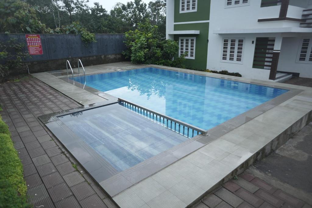 a swimming pool in a yard next to a house at Luxe Hotel - Rooms & Villas Wayanad in Wayanad