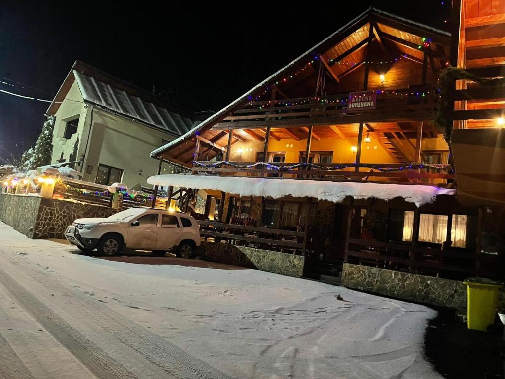 a white car parked in front of a building in the snow at Cabana Loredana in Vadu Moţilor