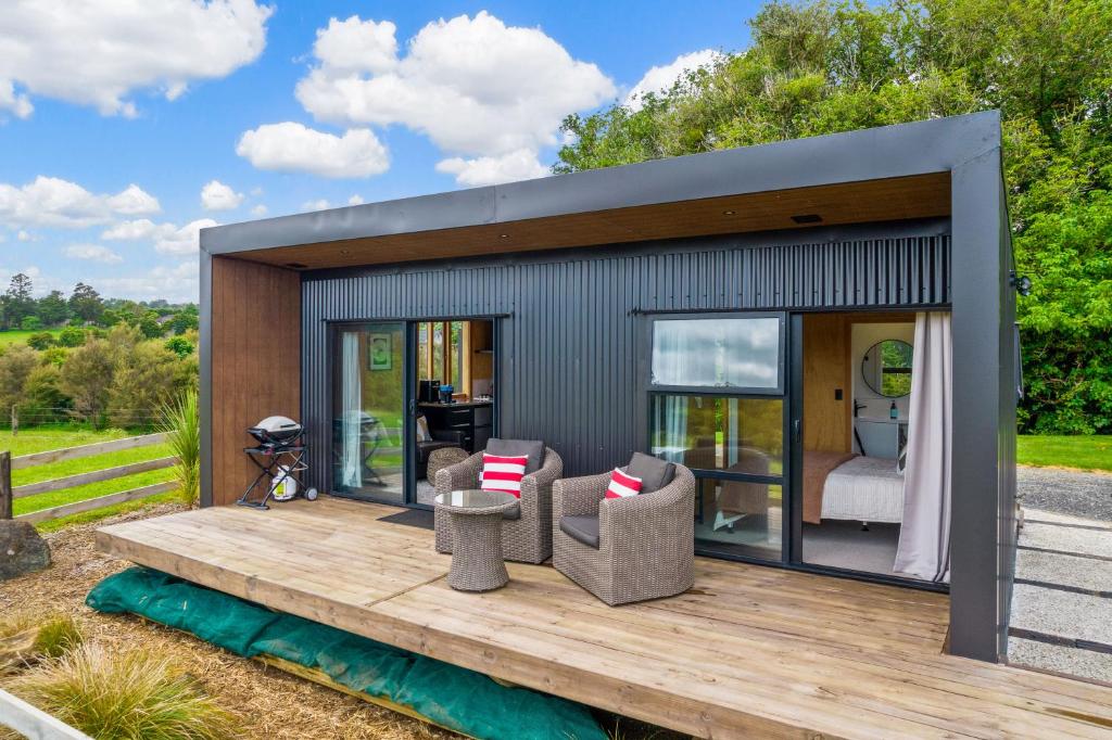 a tiny house on a wooden deck with chairs at Kūkū Kabin - Waimate North Eco Holiday Cabin in Kerikeri