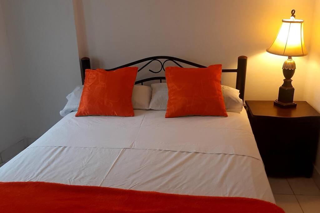 1 cama con almohadas de color naranja y blanco y lámpara en alojamiento cerca centro histórico Popayán., en Popayán
