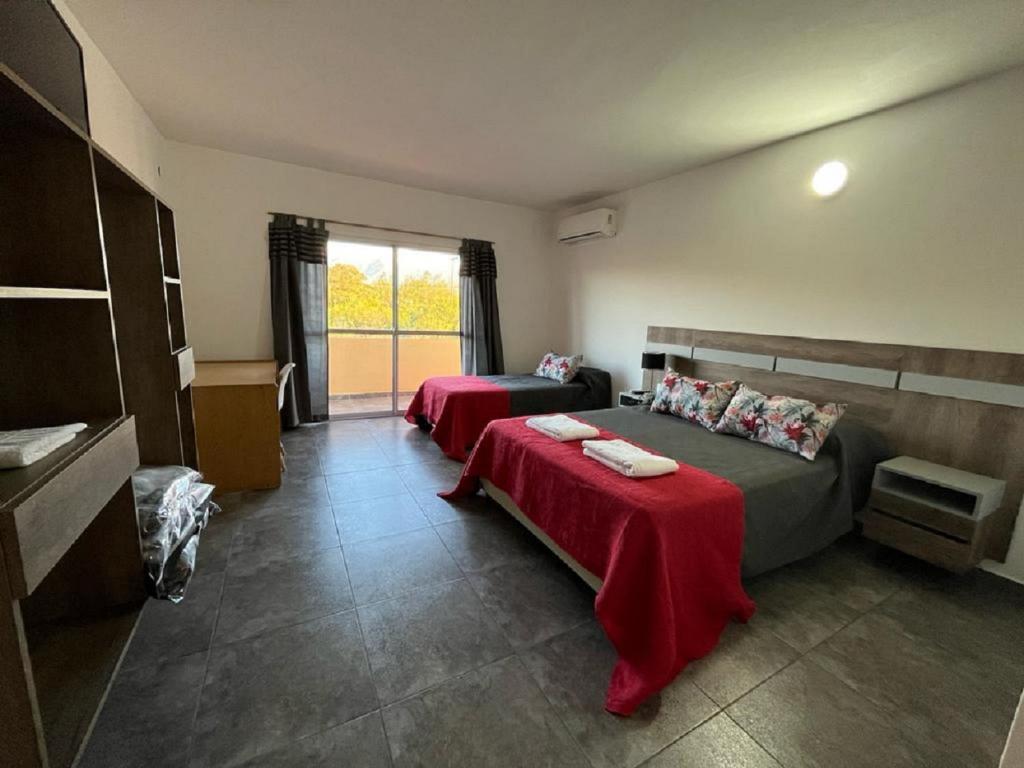 1 Schlafzimmer mit 2 Betten mit roter Bettwäsche und einem Fenster in der Unterkunft Complejo “Aloe Vera” in Villa Dolores