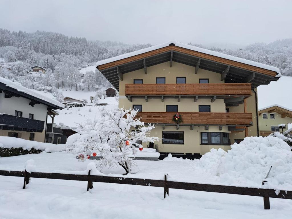 a snow covered house with a tree in front of it at Appartement Reichholf in Bramberg am Wildkogel