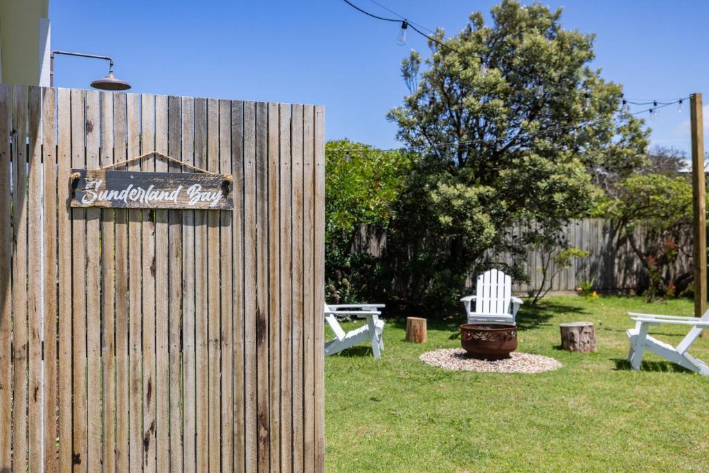 a sign on a fence with two white chairs and a yard at Salt & Stone in Sunset Strip
