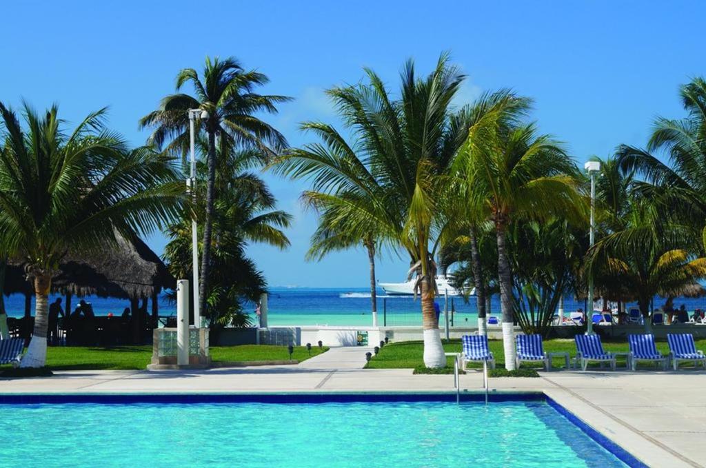 una piscina con palmeras y el océano en Oceanfront condo at voted best Cancun sandy beach, en Cancún