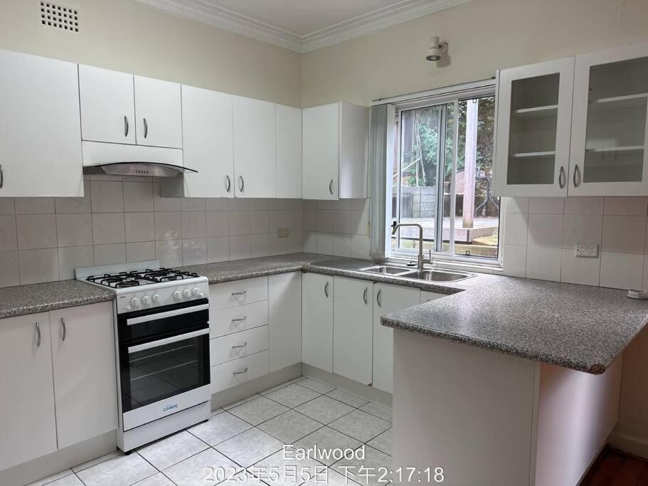 een keuken met witte kasten en een fornuis met oven bij 3 BDR house close to train station, airport & City in Sydney