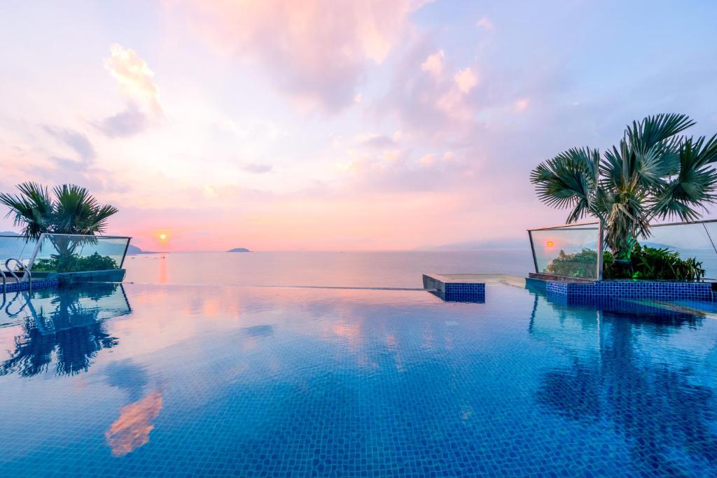 a pool with palm trees and the ocean at sunset at Boton Blue Hotel & Spa in Nha Trang