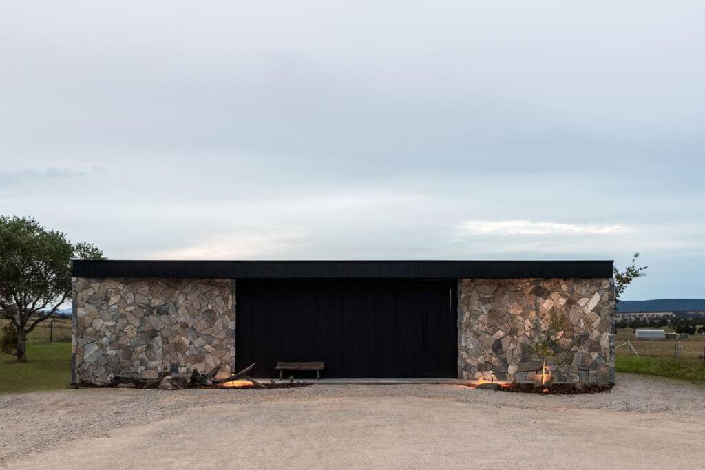 un edificio de piedra con un garaje negro con chimeneas en Zensi Retreat - Villa, en Eurunderee