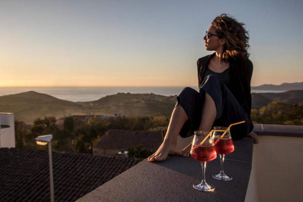 Hotel Maison Tresnuraghes في Tresnuraghes: امرأة تجلس على حافة مع كأسين من النبيذ