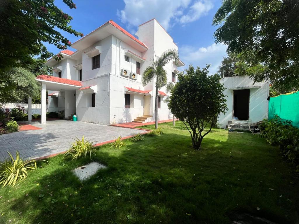 una casa blanca con un césped verde delante de ella en Royal Experiences Pearl House 6 Bed Room Villa with Private Pool, Panayur, en Chennai