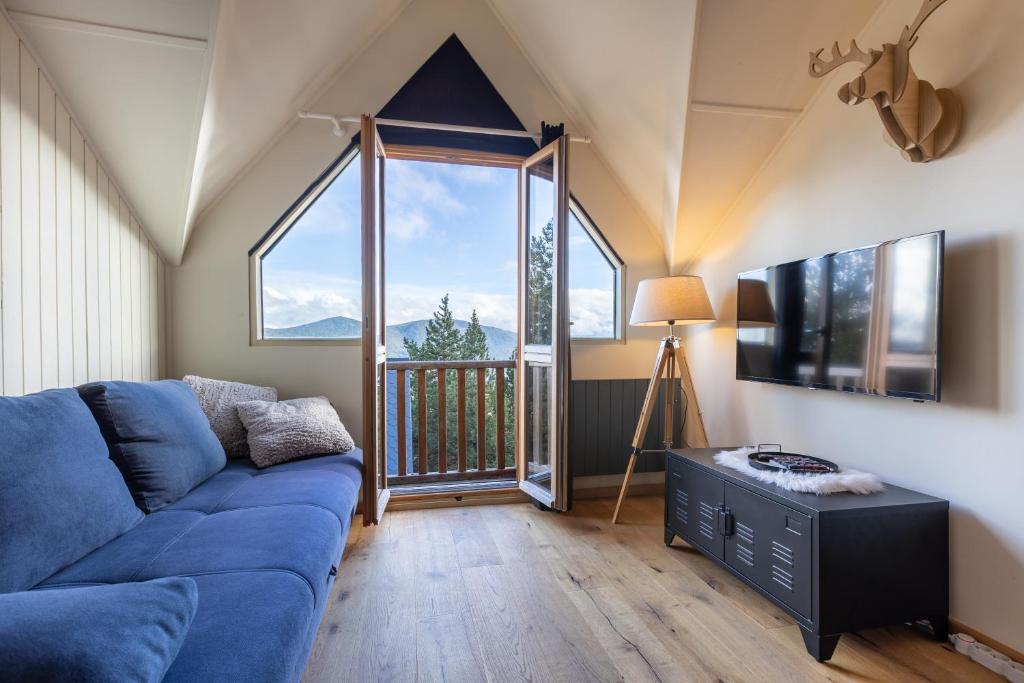sala de estar con sofá azul y ventana grande en Le Cerf - Duplex avec superbe vue montagne, en Les Angles