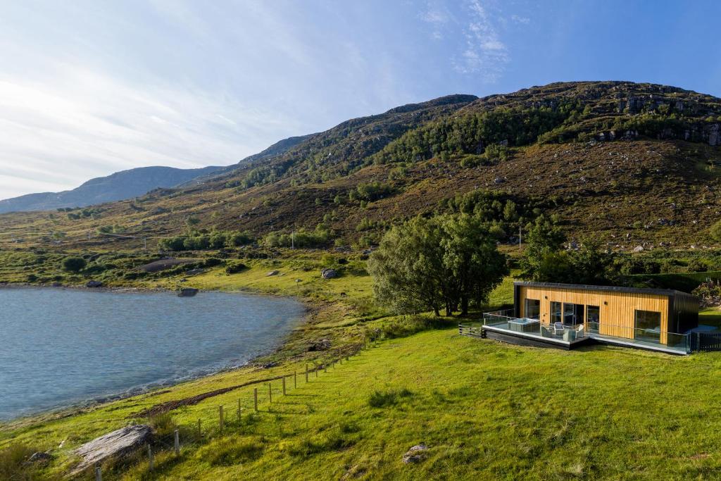 uma casa numa colina ao lado de um corpo de água em Birches Lodge with Hot Tub em Dundonnell