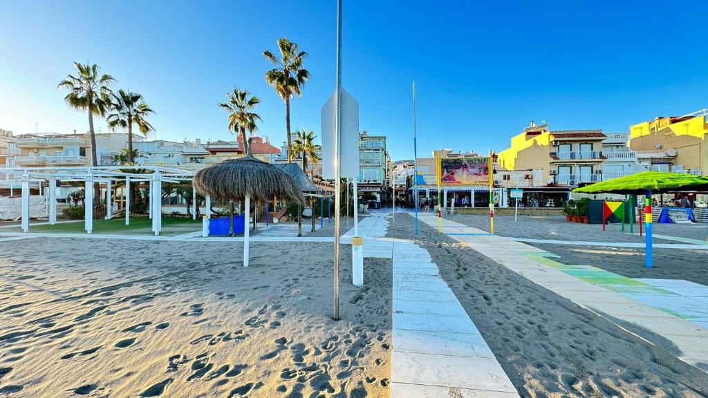 piaszczystą plażę z parasolami i palmami oraz budynkami w obiekcie Carihuela Playa Los Nidos 1 w mieście Torremolinos