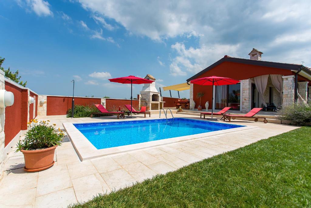 a swimming pool in a yard with red umbrellas at Activity villa Marula with outdoor pool in Buje in Gamboci