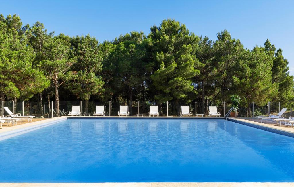a swimming pool with chairs and trees in the background at Hilton Garden Inn Marseille Provence Airport in Marignane