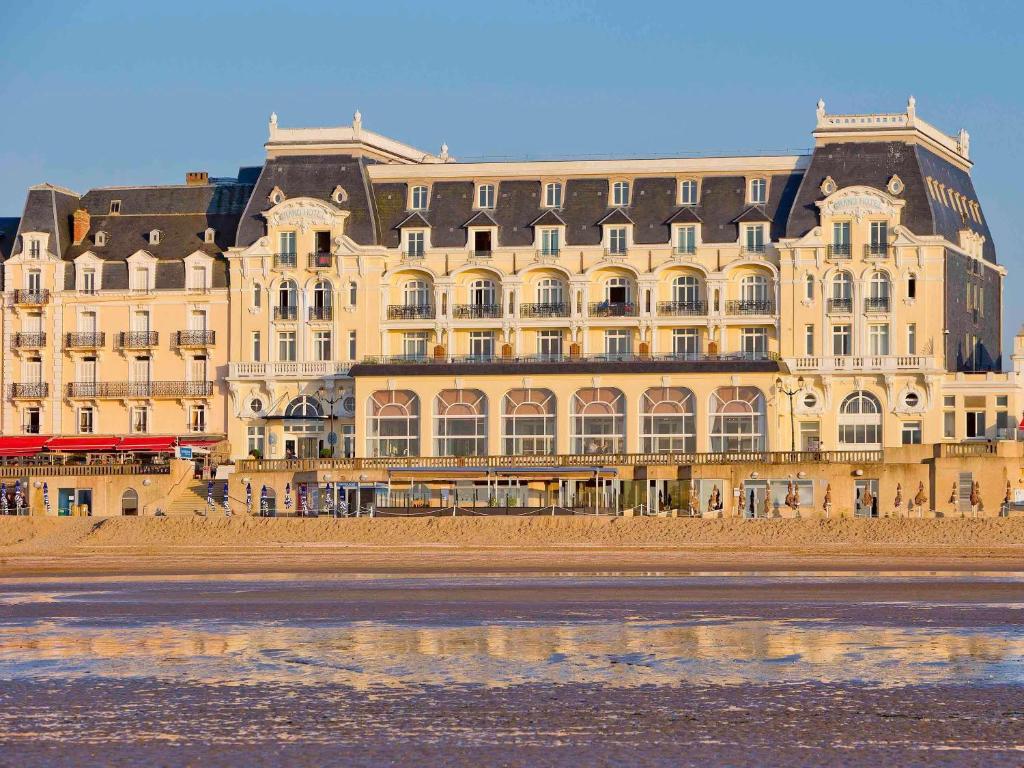 Le Grand Hotel de Cabourg - MGallery Hotel Collection في كابورغ: مبنى كبير على الشاطئ بجوار المحيط