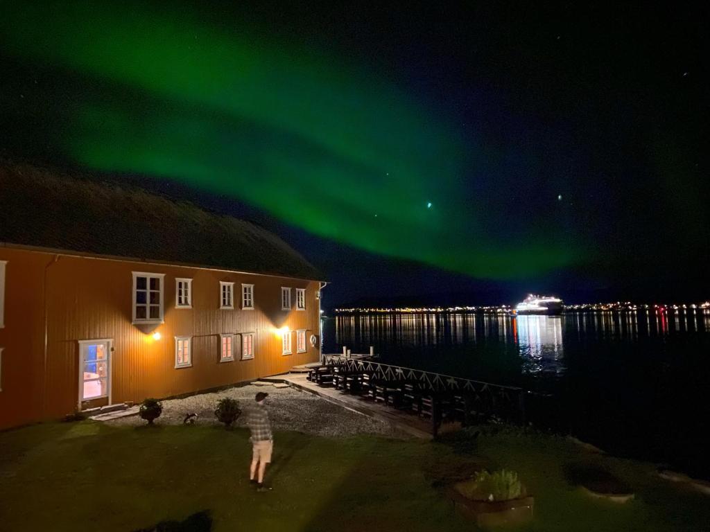 eine Person, die vor einem Haus unter den Nordlichtern steht in der Unterkunft Sandtorgholmen Hotel - Best Western Signature Collection in Harstad