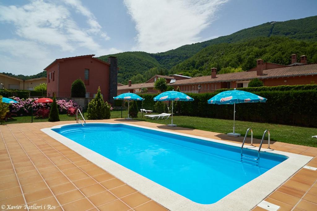 una piscina con sombrillas azules en un patio en Apartamentos Fonda Finet, en Sant Feliu de Pallerols