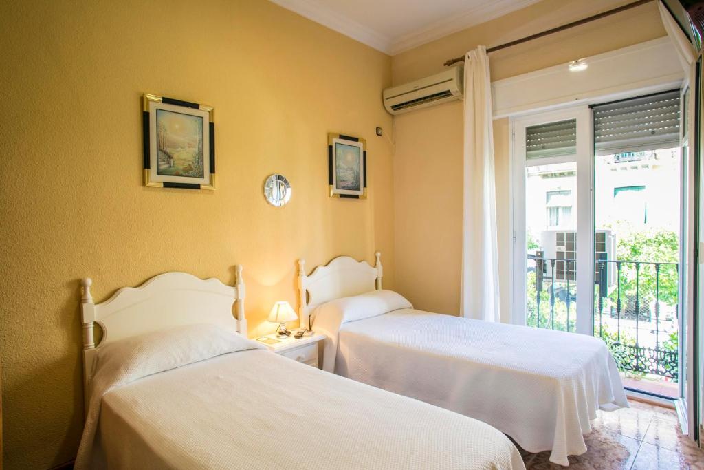 two beds in a room with a window at Pensión Dulces Sueños in Seville