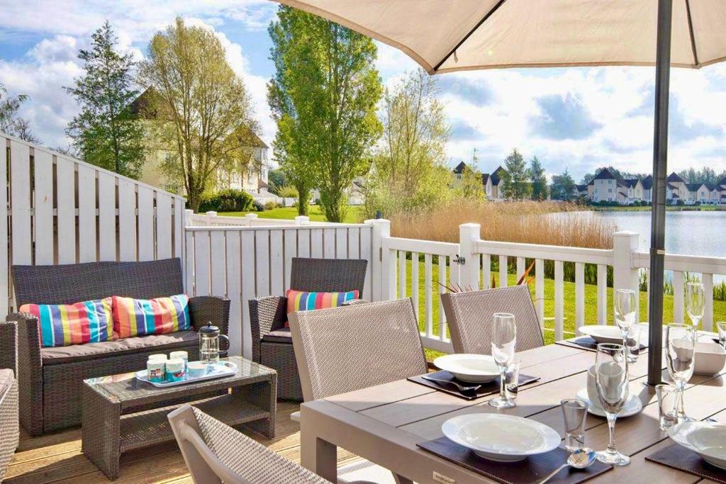 een patio met een tafel en stoelen en een parasol bij Spinnaker Lodge · Cotswolds Lakeside Home in South Cerney