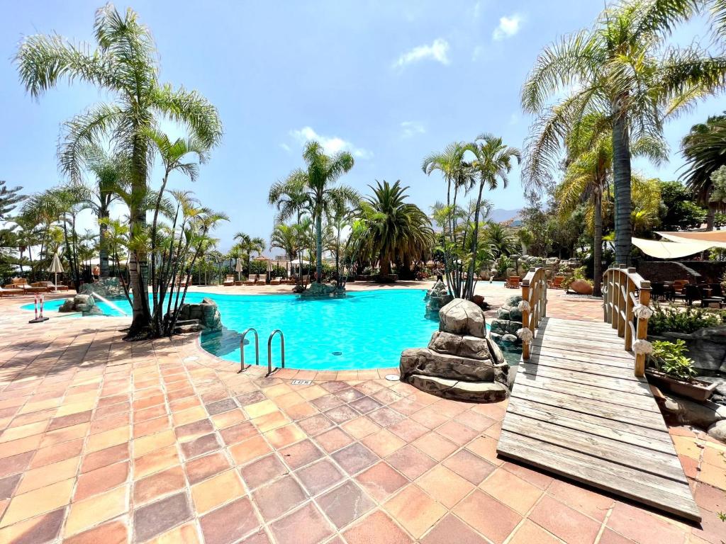 een zwembad in een resort met palmbomen en een houten brug bij Comfortable apartamento AP1, con piscina, cerca de Playa los Roques in Los Realejos