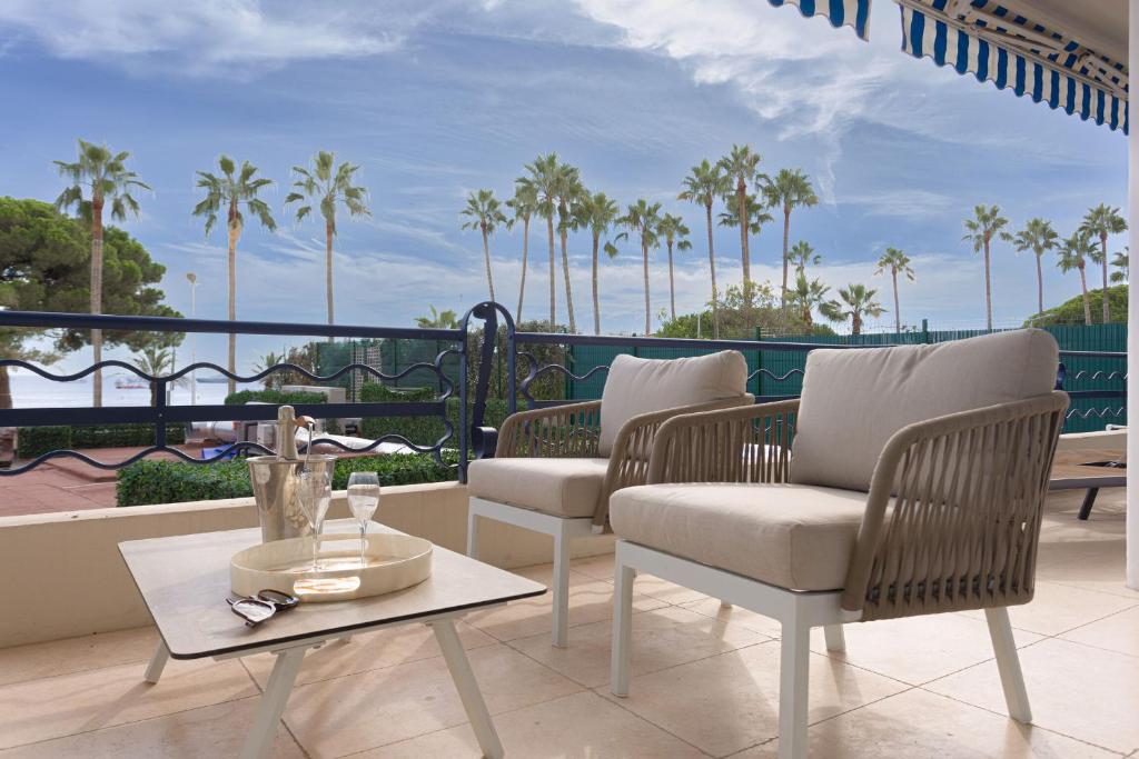 uma varanda com cadeiras, uma mesa e palmeiras em Palais Des Iles - La Croisette em Cannes