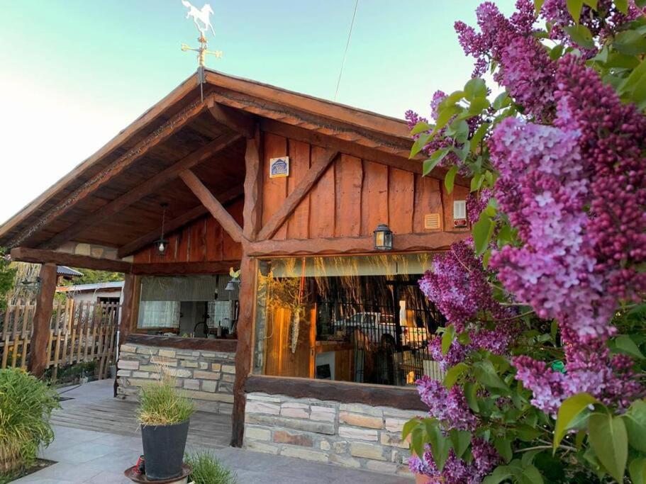 a wooden building with purple flowers in front of it at Sentidos Cardinales in Perito Moreno