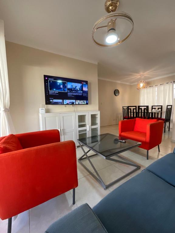 a living room with red chairs and a flat screen tv at Stylish Stay Ciudad Juan Bosch in Los Paredones