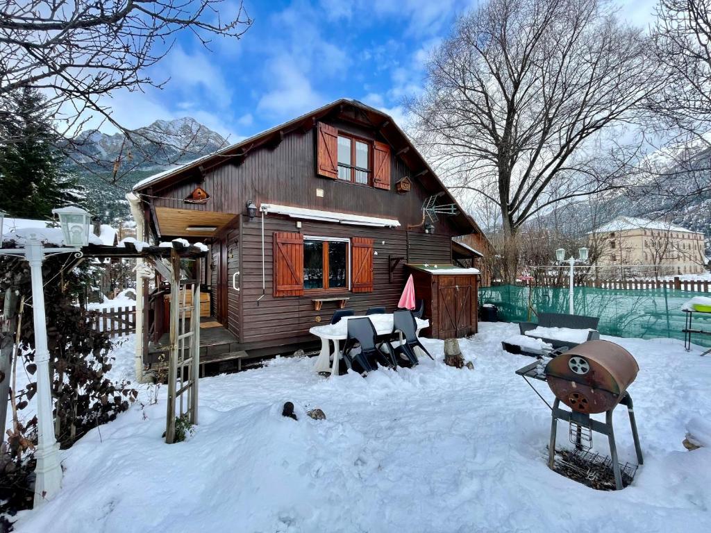 um chalé de madeira na neve com uma mesa e cadeiras em Chalet à proximité de l'Ubaye em Jausiers