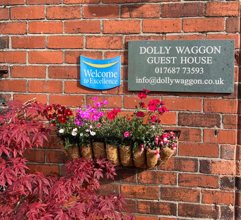 una pared de ladrillo con dos cestas de flores y un cartel en Dolly Waggon Guest House, en Keswick