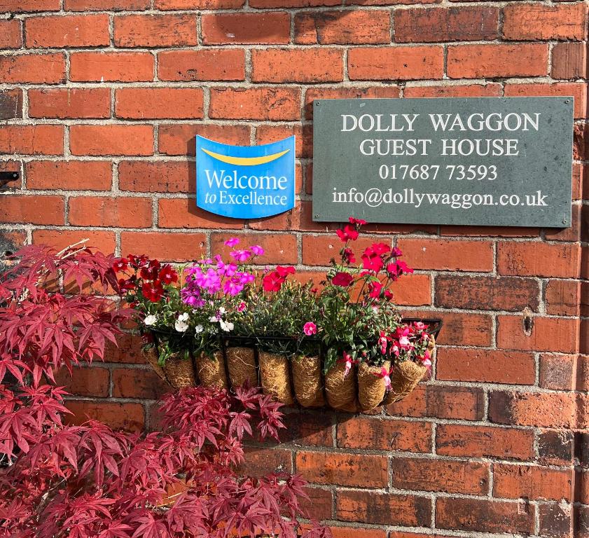 a brick wall with two baskets of flowers and a sign at Dolly Waggon Guest House in Keswick