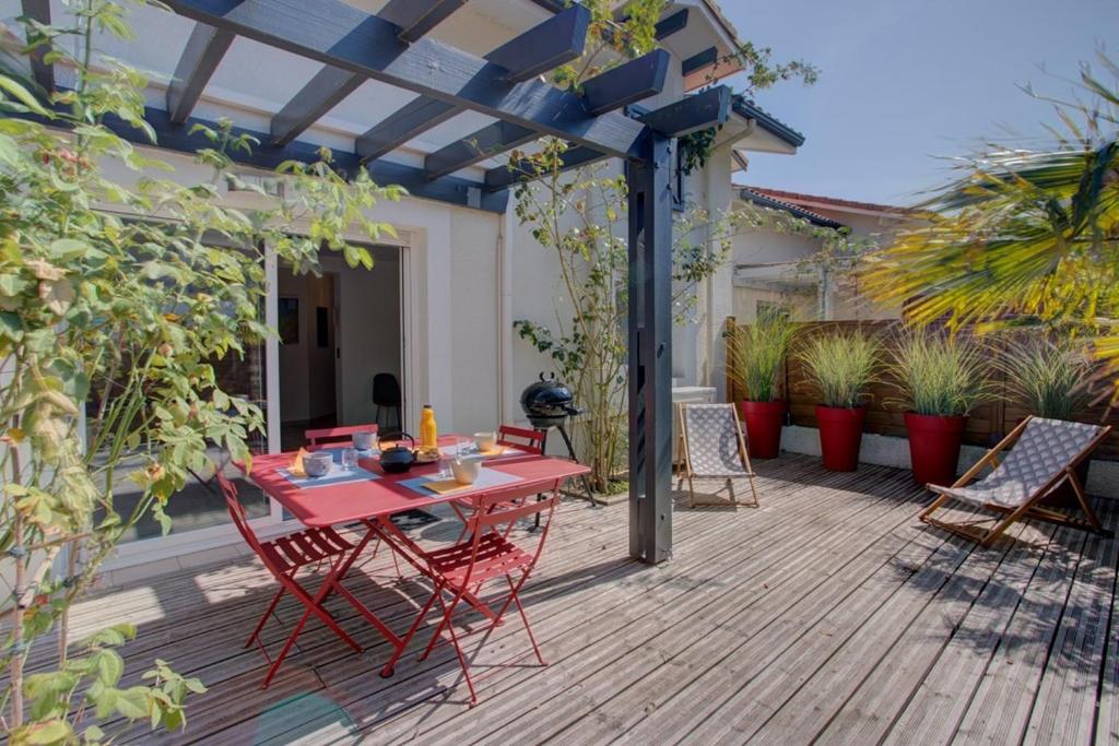 a patio with a red table and chairs on a wooden deck at Biscarrosse Bourg - Duplex avec terrasse classé 3 étoiles in Biscarrosse
