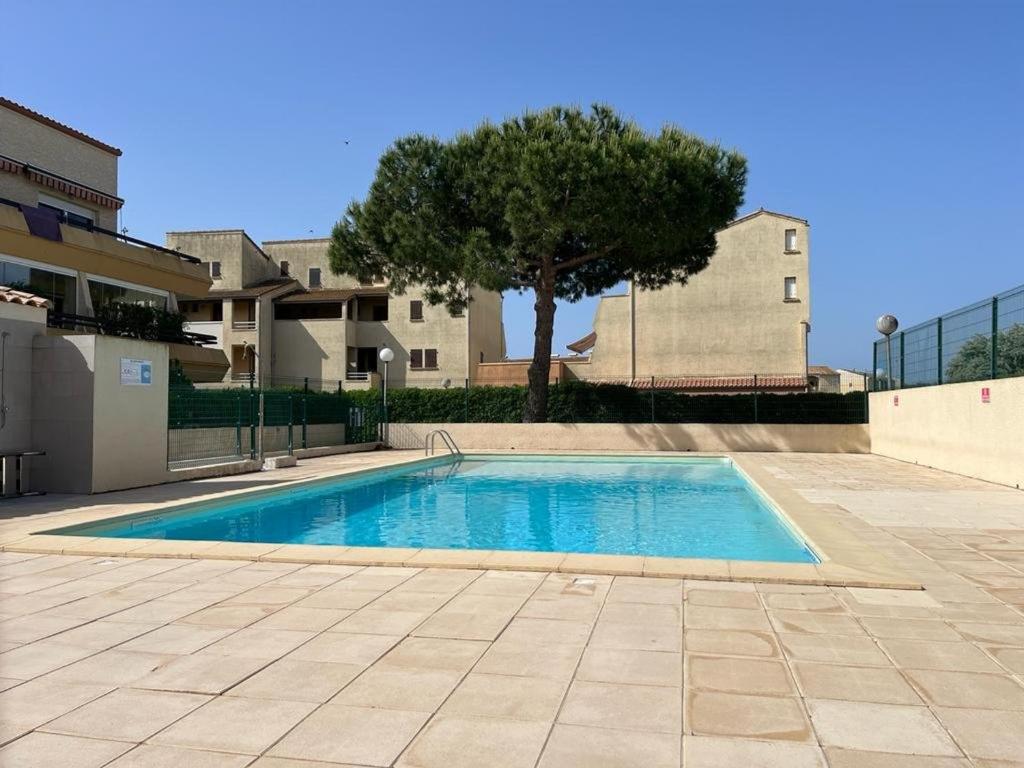 - une piscine dans une cour avec un arbre et un bâtiment dans l'établissement Appartement Rez-de-Jardin: Piscine, Terrasse, Parking, Wi-Fi en Option - FR-1-387-63, à Marseillan