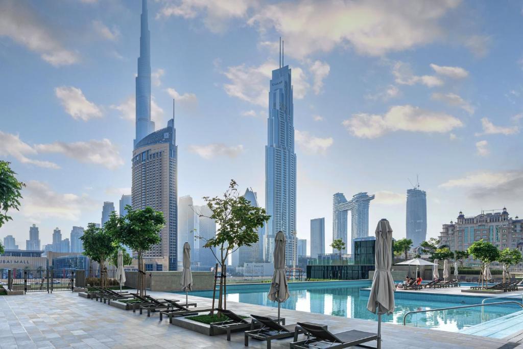 une piscine avec des chaises et des parasols et une vue sur la ville dans l'établissement Sleeps 8 Burj Views Direct Dubai Mall Access, à Dubaï