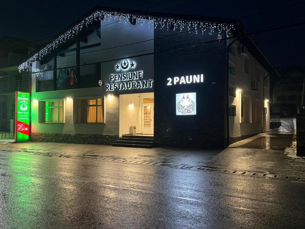 a building with a sign on the side of it at night at Pensiune Restaurant Pizzerie 2 Păuni in Borşa