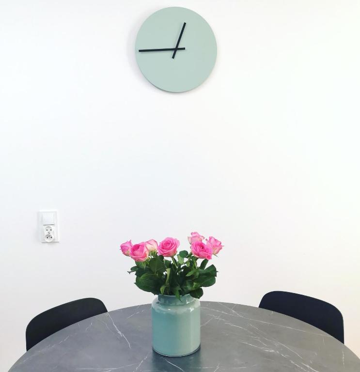 a vase with pink roses on a table with a clock at Plażowa Park Apartamenty in Międzywodzie