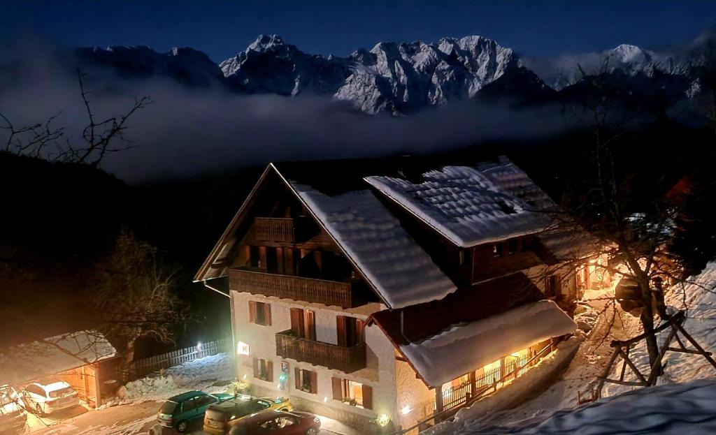 una casa en la nieve por la noche con montañas nevadas en Farm Stay "Alpine Dreams" en Solčava