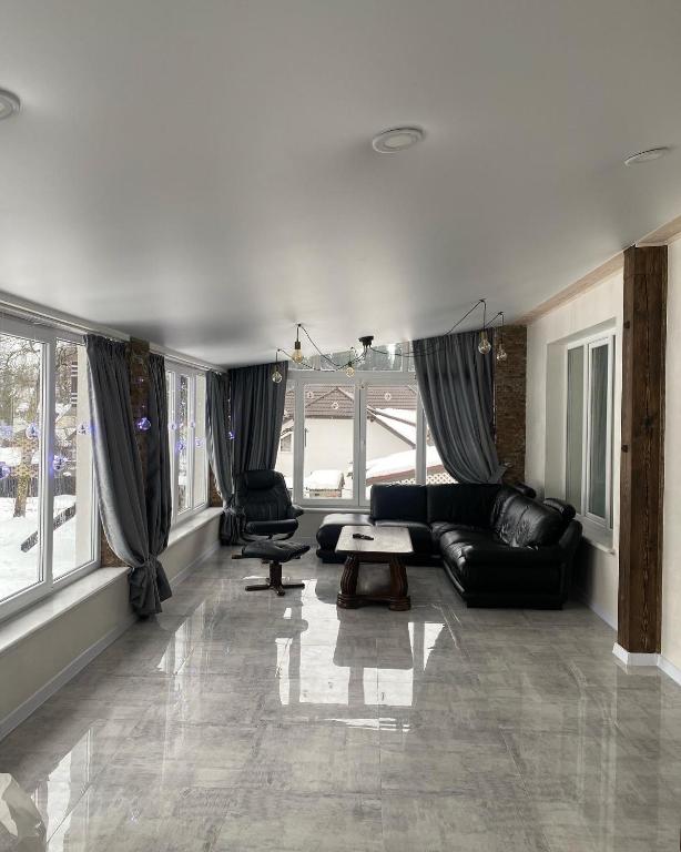 a living room with black leather furniture and large windows at Котедж Смерекова хата- Пилипець in Kelechin