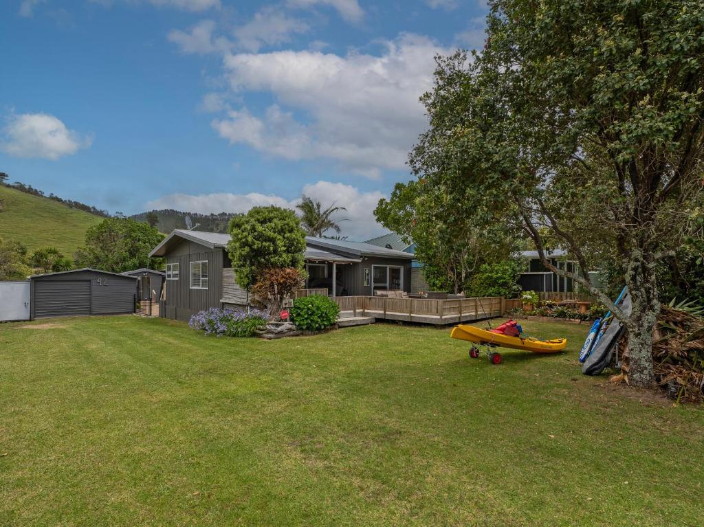 a house with a yard with two boats on the grass at Kon Tiki Retreat - Whiritoa Beach Holiday Home in Whiritoa