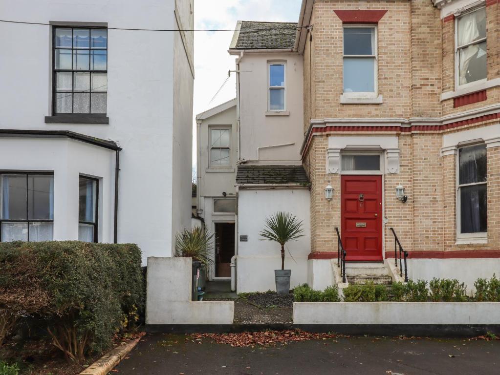 une maison avec une porte rouge dans une rue dans l'établissement Mimosa, à Dawlish