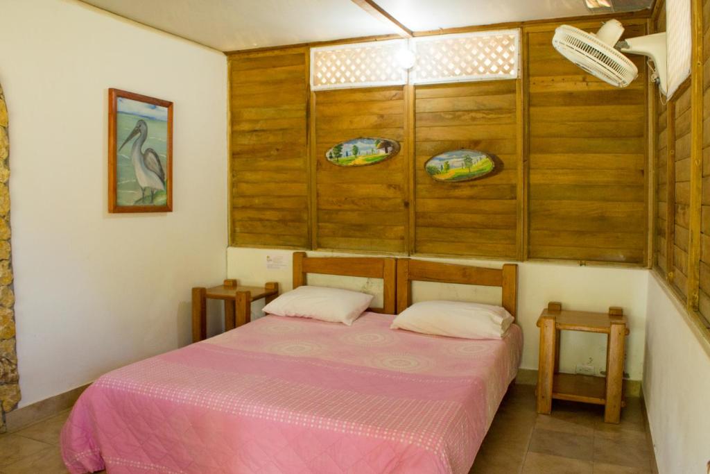 una piccola camera con un letto rosa e due tavoli di Hotel Rancherío Shangai a Moñitos