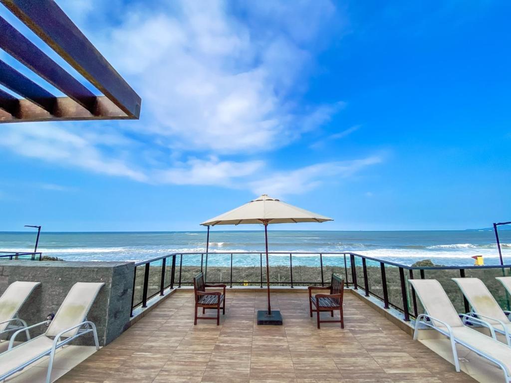 eine Terrasse mit Stühlen und einem Sonnenschirm am Strand in der Unterkunft Resort em Barra velha, pé na areia e vista mar in Barra Velha