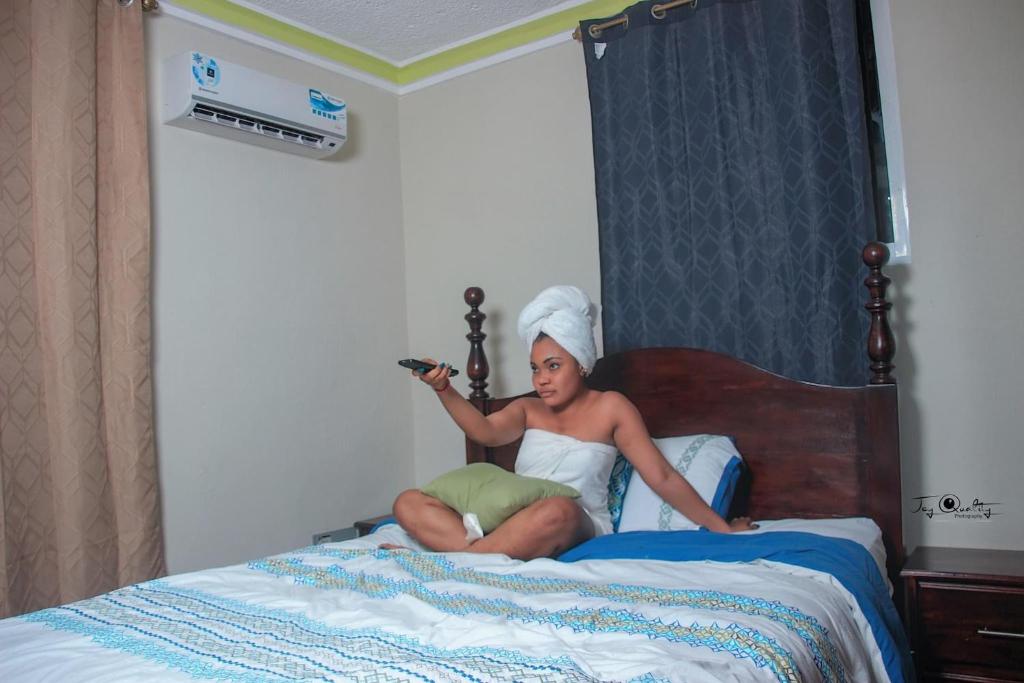 uma mulher sentada numa cama segurando um controle remoto em Le Bigot Appartements em Marotte